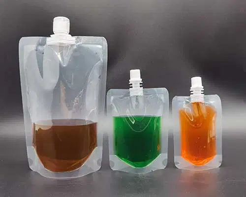 Transparent spouted liquid packaging bags in different sizes, containing brown, green and orange liquids respectively.